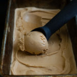 Vietnamese coffee ice-cream in a metal container with an ice-cream scoop.