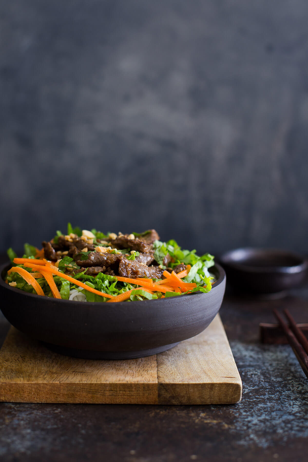Bowl of Vietnamese lemongrass beef with noodles, lettuce, and shredded carrots.