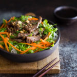 Bowl of Vietnamese lemongrass beef with noodles, lettuce, and shredded carrots.