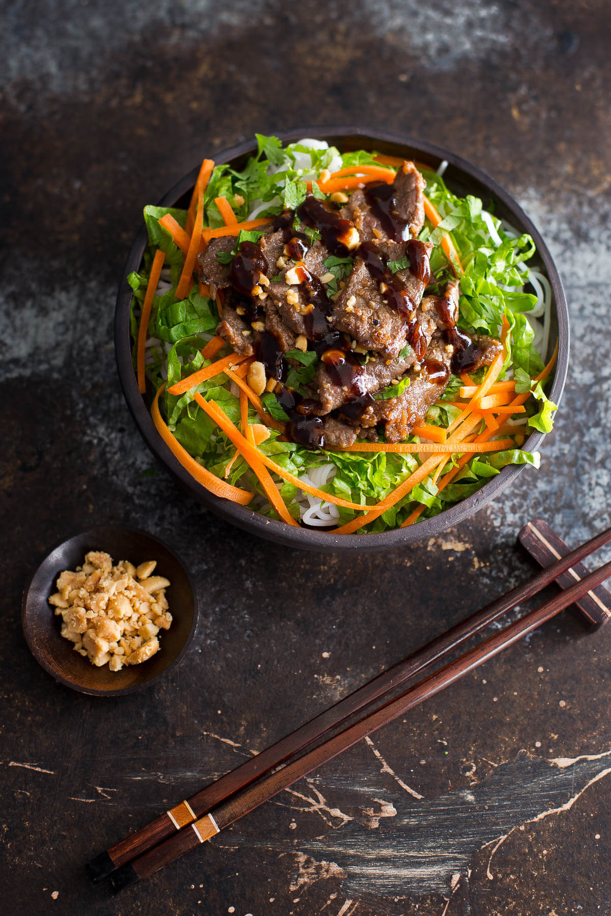 Bowl of Vietnamese lemongrass beef with noodles, lettuce, and shredded carrots topped with garlic hoisin sauce and crushed peanuts.