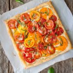 Tomato tart with goat cheese and caramelized onions on a piece of parchment paper with loose basil leaves.