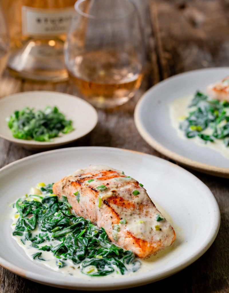 A plate of pan seared salmon with creamed spinach on the side shown with a bottle of Rosé wine and a wine glass.