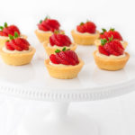 Several mini strawberry tartlets on a white cake stand.