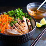 Vietnamese noodles with marinated grilled chicken in a bowl served with fresh lettuce, herbs, and fish sauce.