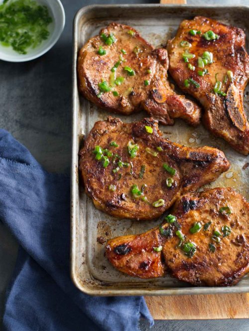 Top view of sheet pan with Vietnamese pork chops, dish of scallion oil, and blue napkin.