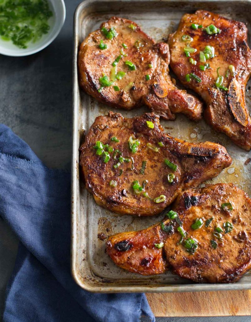 Top view of sheet pan with Vietnamese pork chops, dish of scallion oil, and blue napkin.