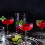 Several glasses of sparkling ginger pomegranate mocktail on a dark table.