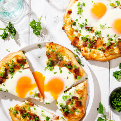 Overhead view of two breakfast pizzas on a white board.