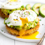 A fried green tomato topped with avocado and a poached egg on a white plate.