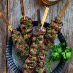 Overhead view of several lemongrass beef skewers on a metal serving dish.