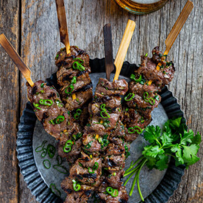 Overhead view of several lemongrass beef skewers on a metal serving dish.