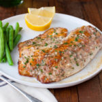 Tilapia fillet, green beans, and lemon wedges on a white plate.