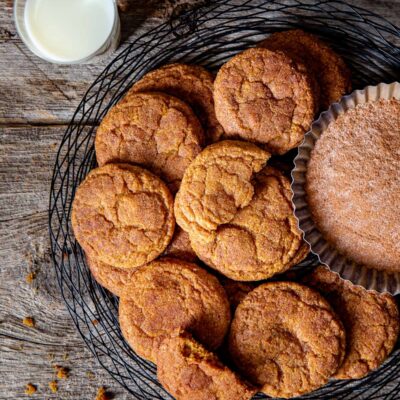 Overhead view of pumpkin snickerdoodle cookies on a black wire tray next to some cinnamon-sugar.