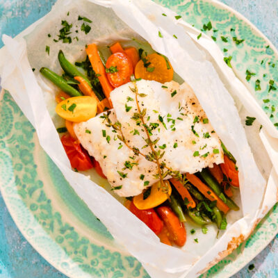 Close-up of fish fillet and vegetables in a parchment paper packet.