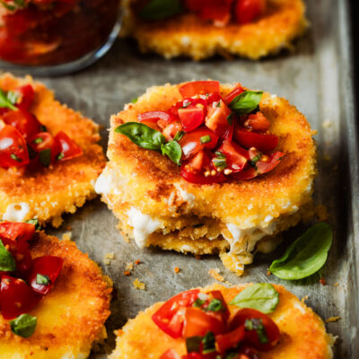 Stack of fried mozzarella slices topped with tomatoes and basil.