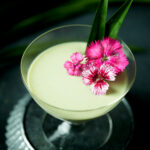 Pandan panna cotta in a glass garnished with pink flowers.