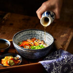 Dashi broth being poured into a bowl of salmon and rice.