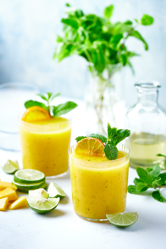 Frozen mango mojito garnished with a dried orange slice and mint.