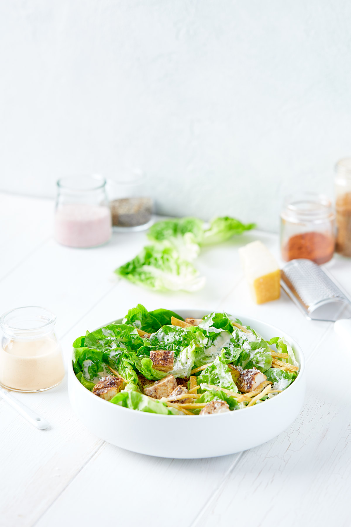 Serving bowl containing chicken caesar salad next to jar of dressing.