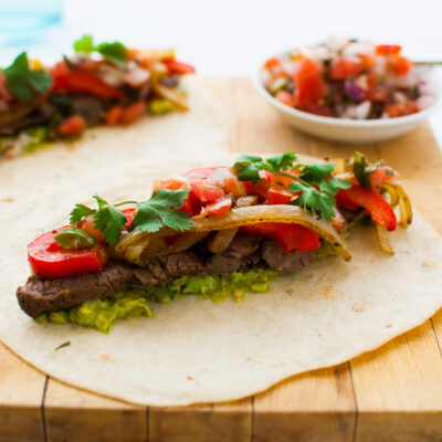 Fajita beef, onions, bell peppers, guacamole, and cilantro on a flour tortilla.