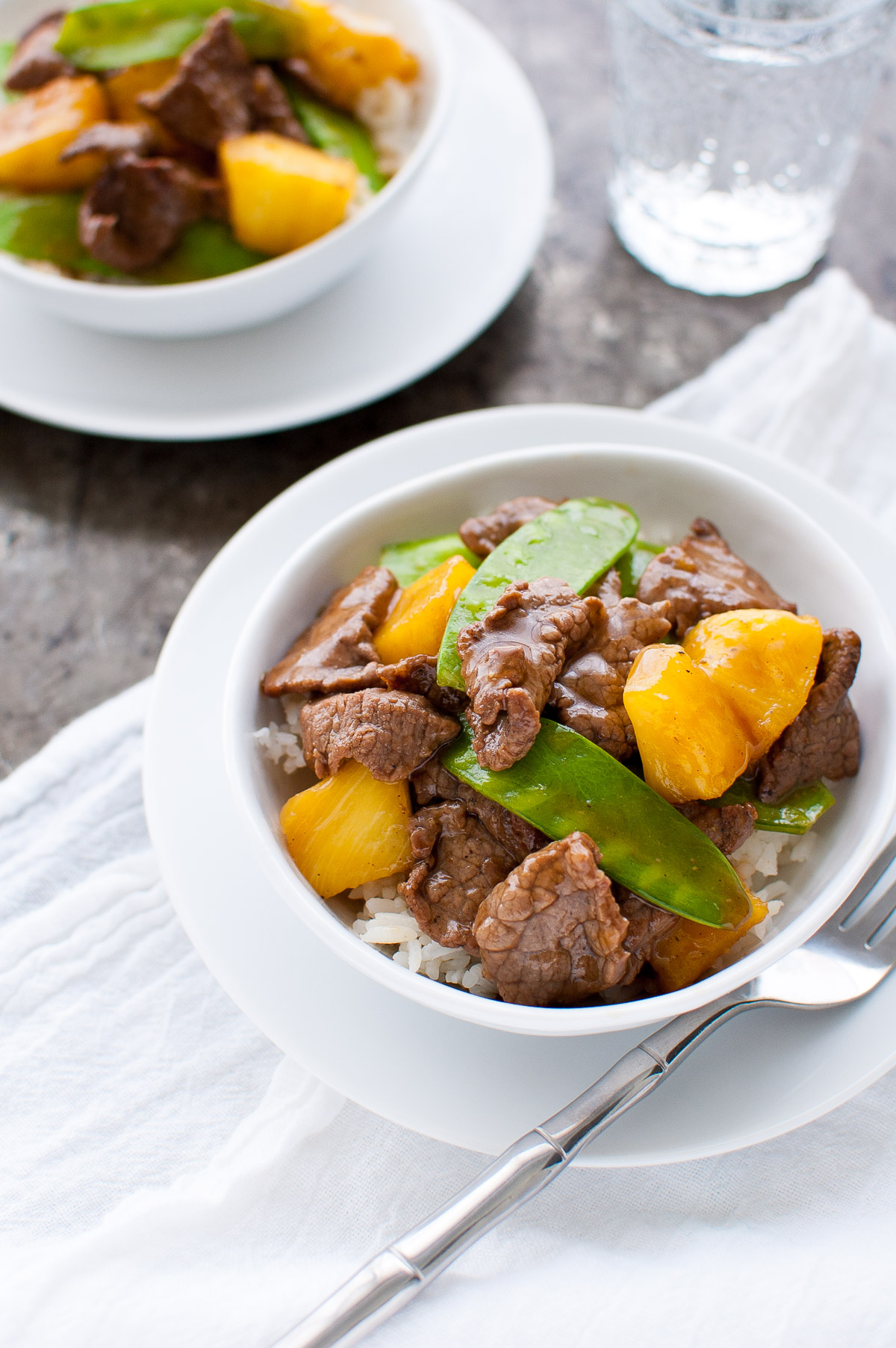 Top down view of beef, pineapple, and snow peas stir-fry in a white bowl.