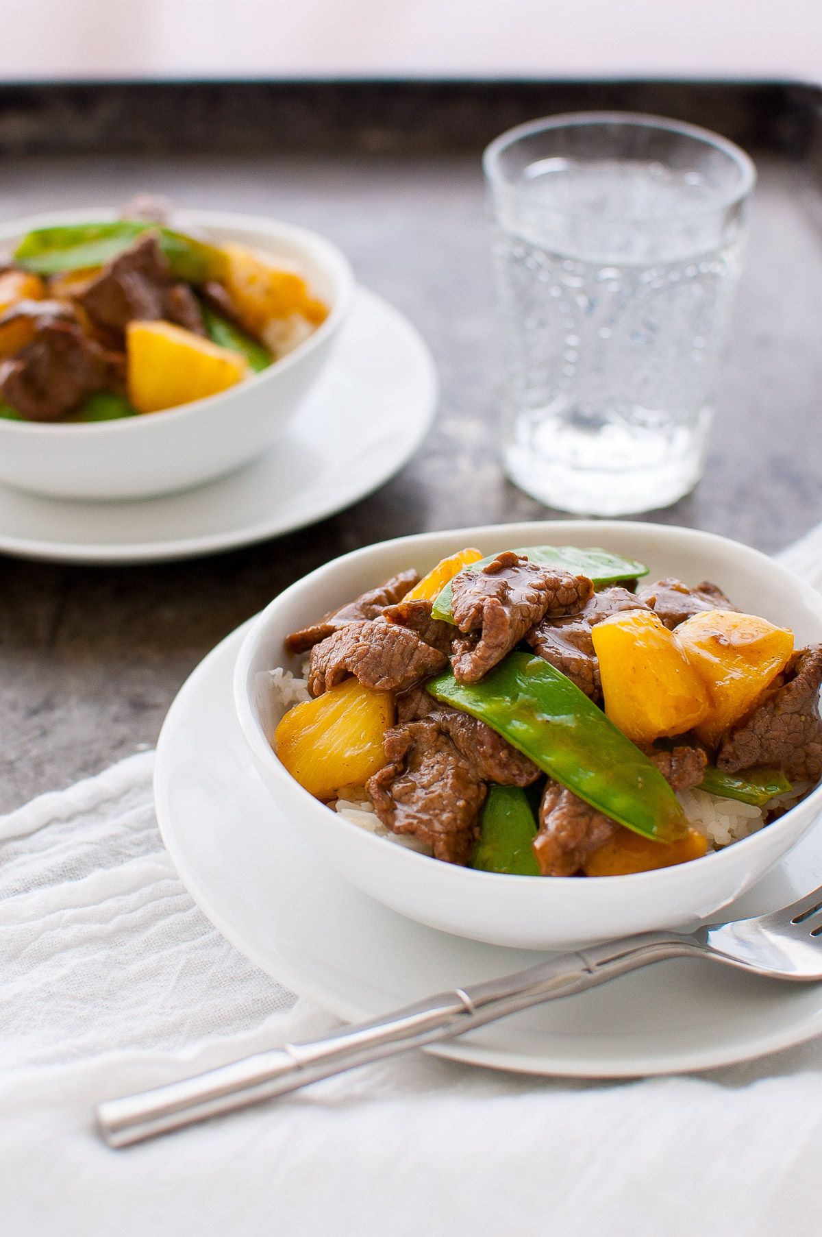 Beef, pineapple, and snow peas stir-fry in a white bowl.