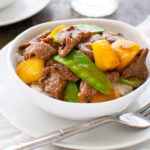 Beef, pineapple, and snow peas stir-fry in a white bowl.