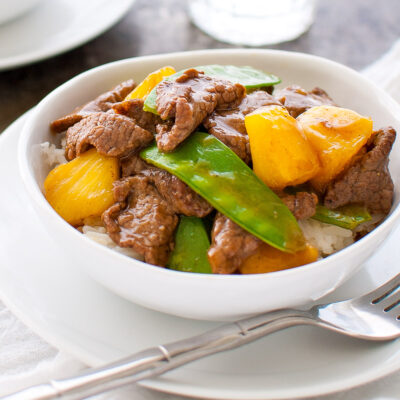 Beef, pineapple, and snow peas stir-fry in a white bowl.
