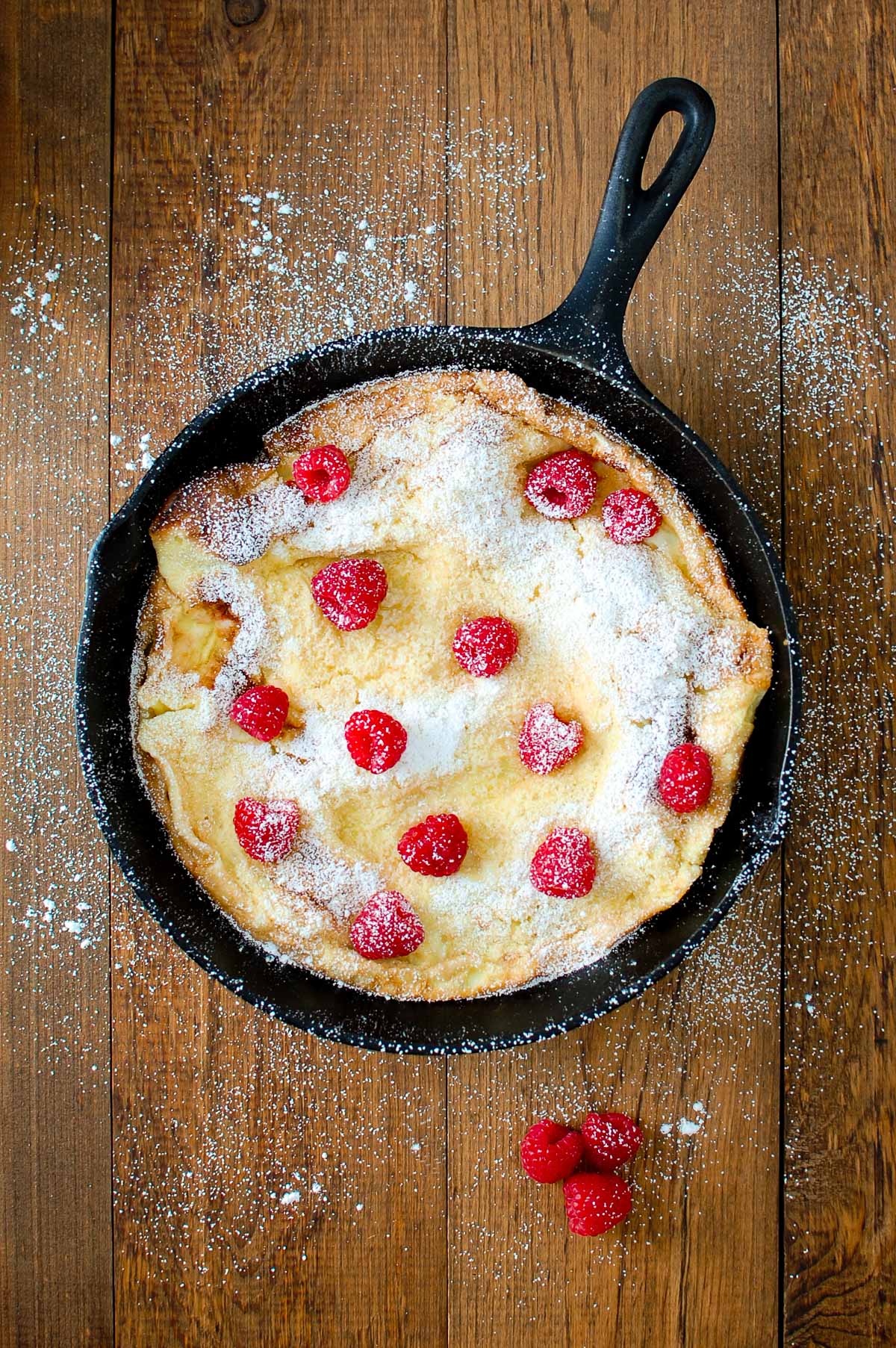 Pear dutch baby sprinkled with powdered sugar and topped with raspberries.