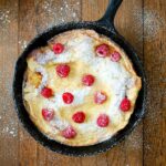 Pear dutch baby sprinkled with powdered sugar and topped with raspberries.