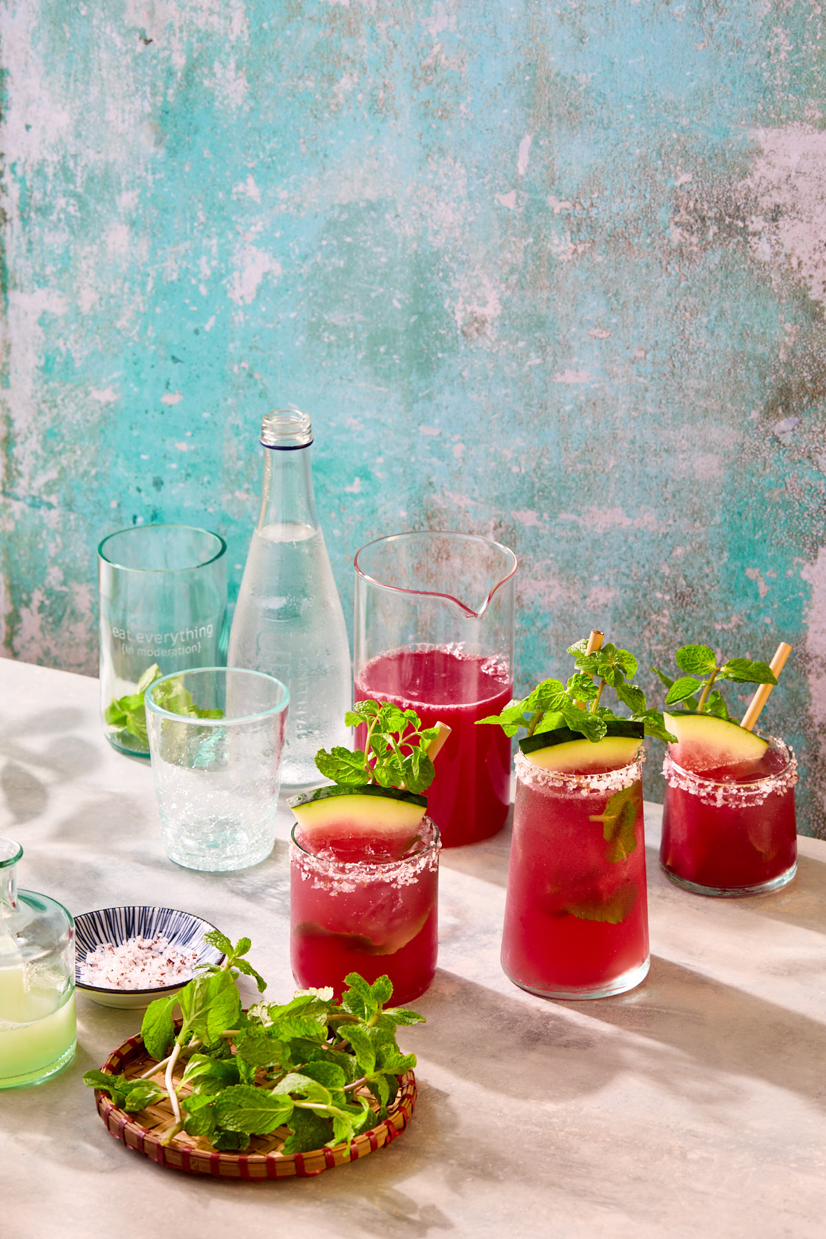 Several glasses of watermelon mocktails with fresh mint, lime juice, and bottle of sparkling water.