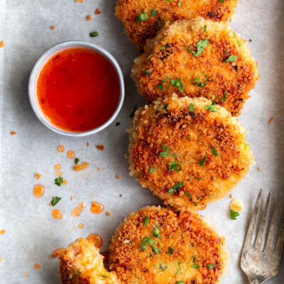 Salmon cakes on parchment paper with a small bowl of sweet chili sauce on the side.