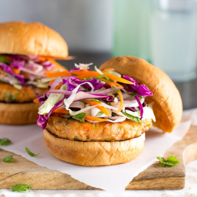 A salmon burger topped with cabbage slaw on a wooden board with a bottle of lemonade in the background.