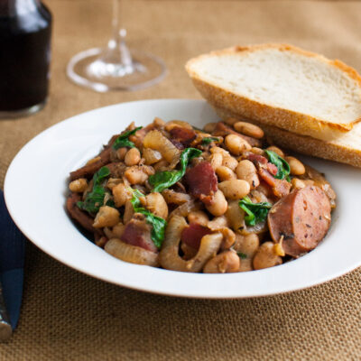 White bean stew in a white bowl next to a glass of red wine.