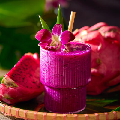 Glass of dragonfruit mocktail next to a cut piece of dragonfruit.