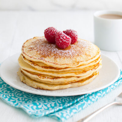 A stack of lemon soufflé pancakes garnished with powdered sugar and fresh raspberries on a white plate.