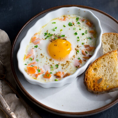 A baked egg topped with chopped chives in a white ramekin next to some toast.