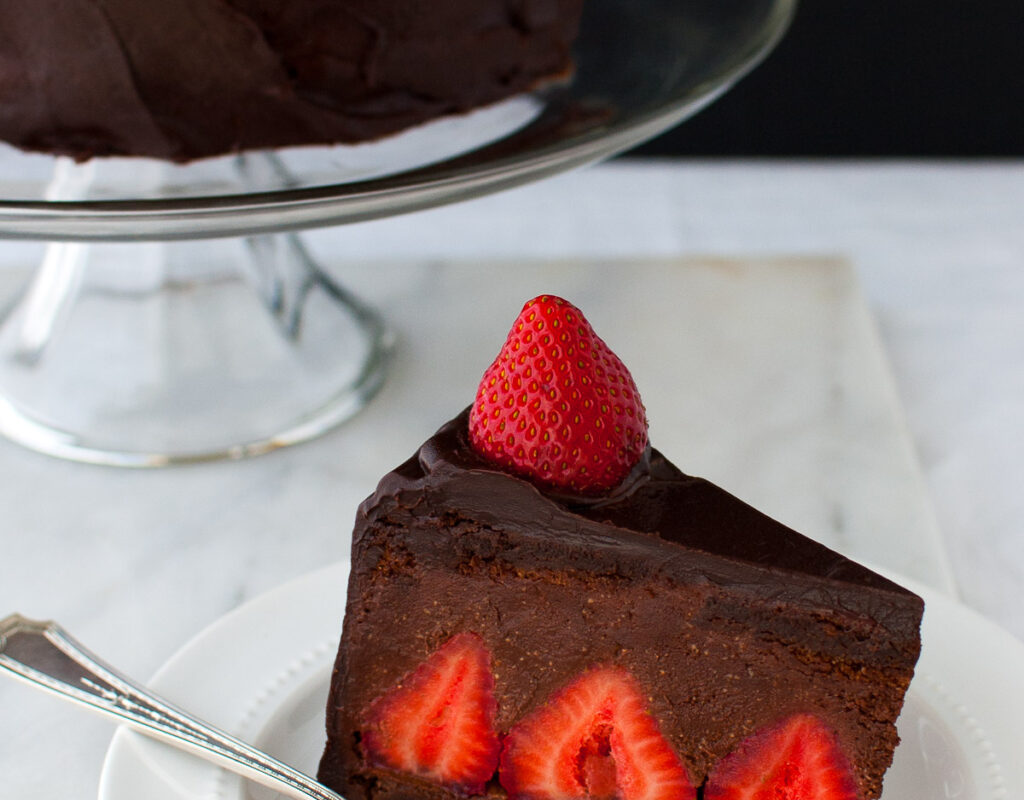 A slice of chocolate strawberry mousse cake on a white plate in front of a cake stand.