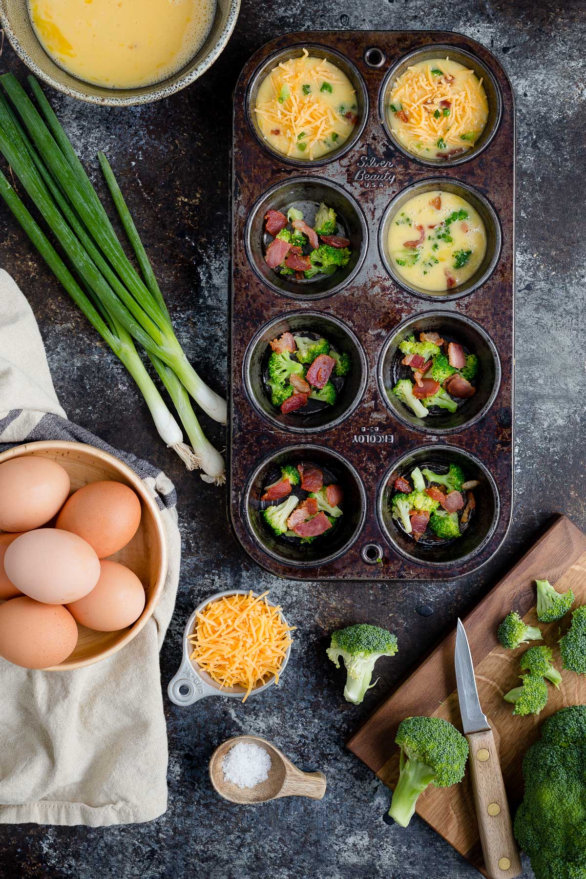 A muffin tin with frittata fillings laid out on a wooden board.