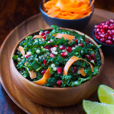 Pomegranate, Israeli couscous and kale salad in a wooden bowl.