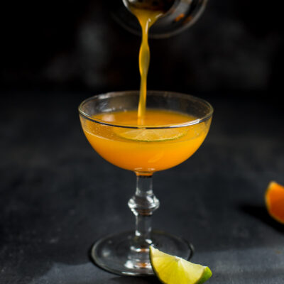 Orange vodka cocktail being poured from a shaker into a coupe glass.