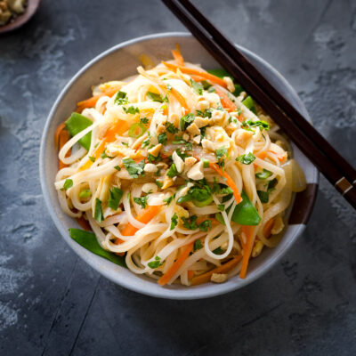 A bowl of chicken and veggie pad thai garnished with chopped herbs and peanuts.