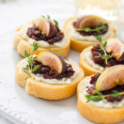 Fig and goat cheese crostini on a white plate.