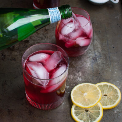 Sparkling water being poured into a glass of hibiscus ginger tea spritzer.