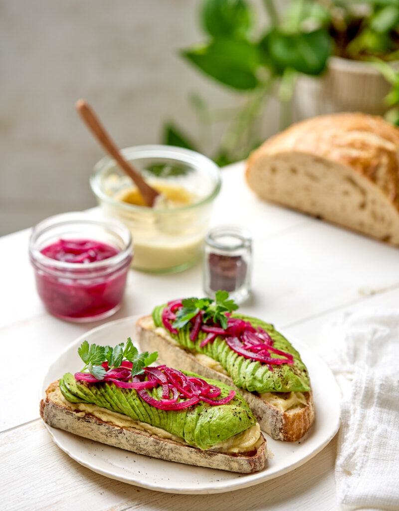 Two slices of avocado toast on a white table next to a white napkin.