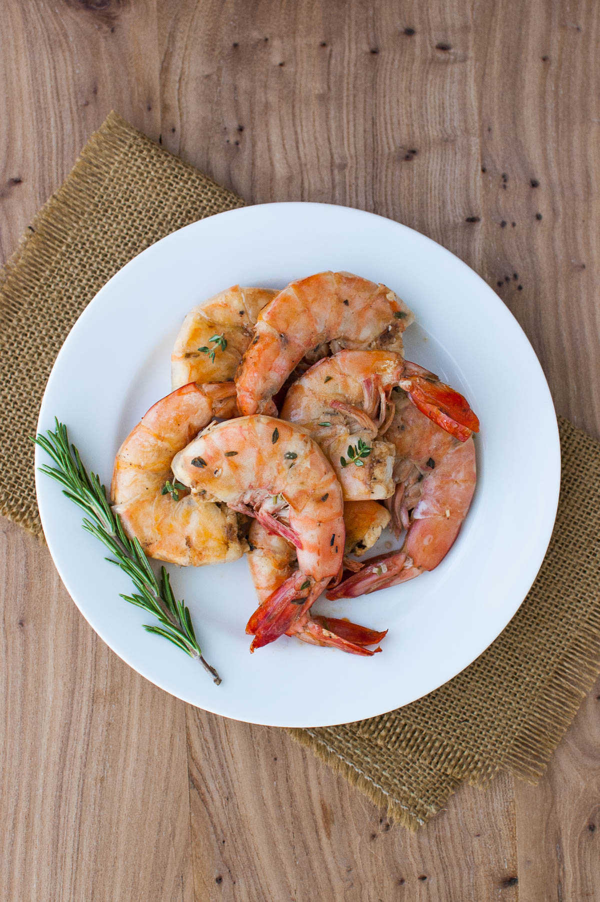 Lemon and herb grilled shrimp on a white plate on a brown placemat.