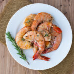 Lemon and herb grilled shrimp on a white plate on a brown placemat.