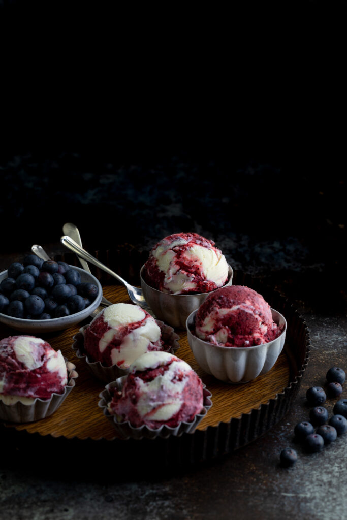 Scoops of blueberry sorbet vanilla swirl ice-cream in metal bowls on a serving tray with some fresh blueberries.