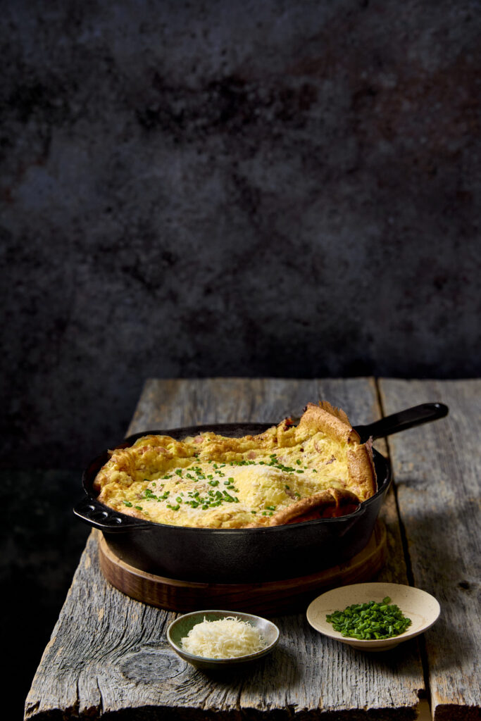Ham and onion dutch baby on a wooden table.