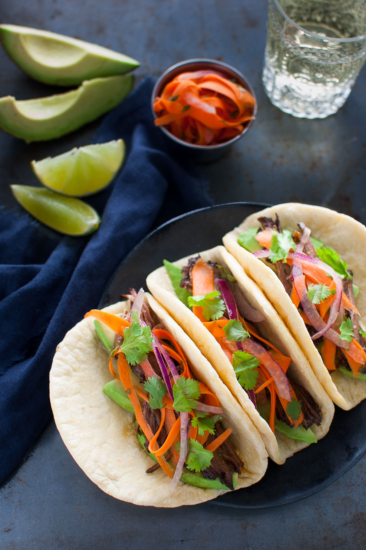 Three Korean beef tacos on a black plate.
